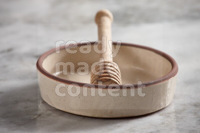 Beige Pottery Oven Bowl with wooden honey handle on the side with grey marble flooring, 15 degree angle
