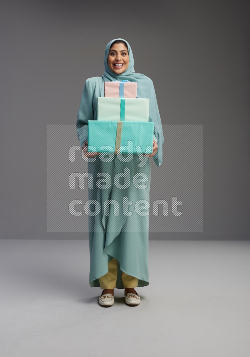 Saudi Woman wearing Abaya standing holding gift box on Gray background