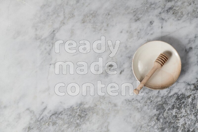 طبق فخاري بيج مع ملعقة عسل خشبية بداخله على خلفية من الرخام الرمادي