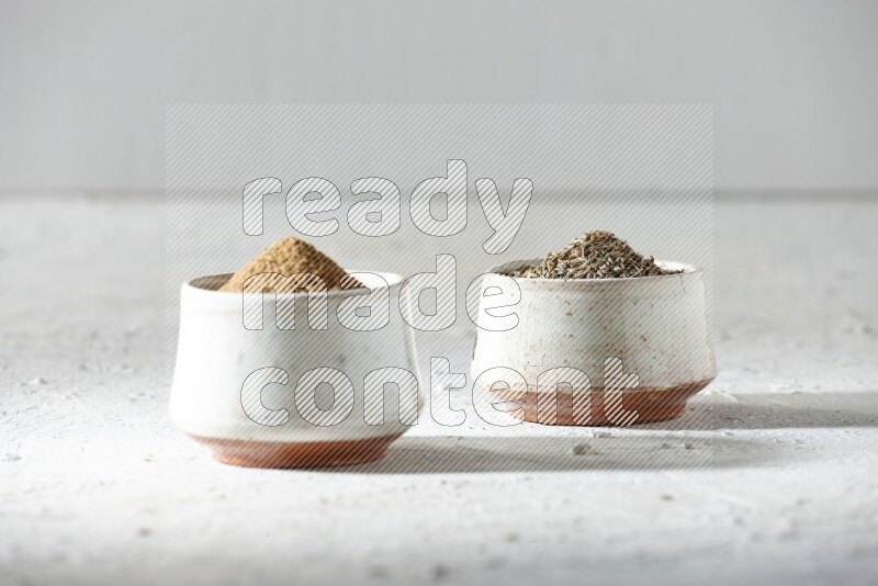 2 beige bowls full of cumin seeds and powder on a textured white flooring