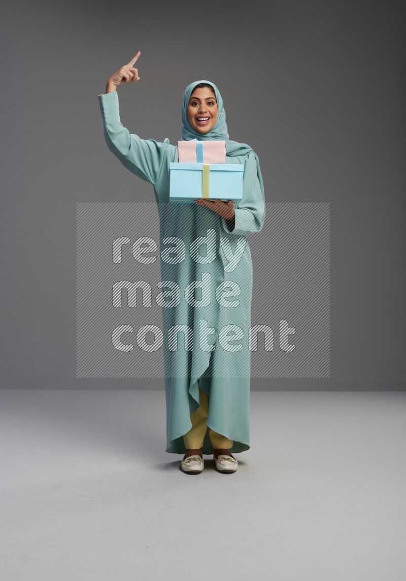 Saudi Woman wearing Abaya standing holding gift box on Gray background