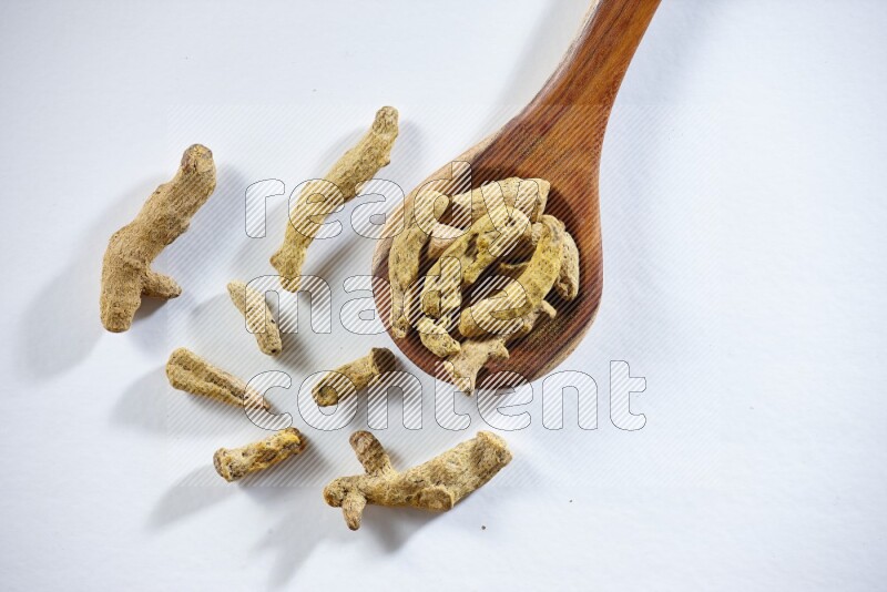 A wooden ladle full of dried turmeric fingers on white flooring