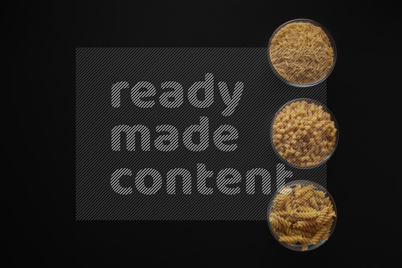 Different pasta types in 3 glass bowls on black background
