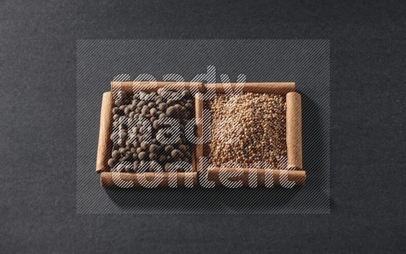 مربعان من أعواد القرفة ممتلئان بحبوب الخردل وحبوب بهار الفلفل الحلو علي خلفية سوداء