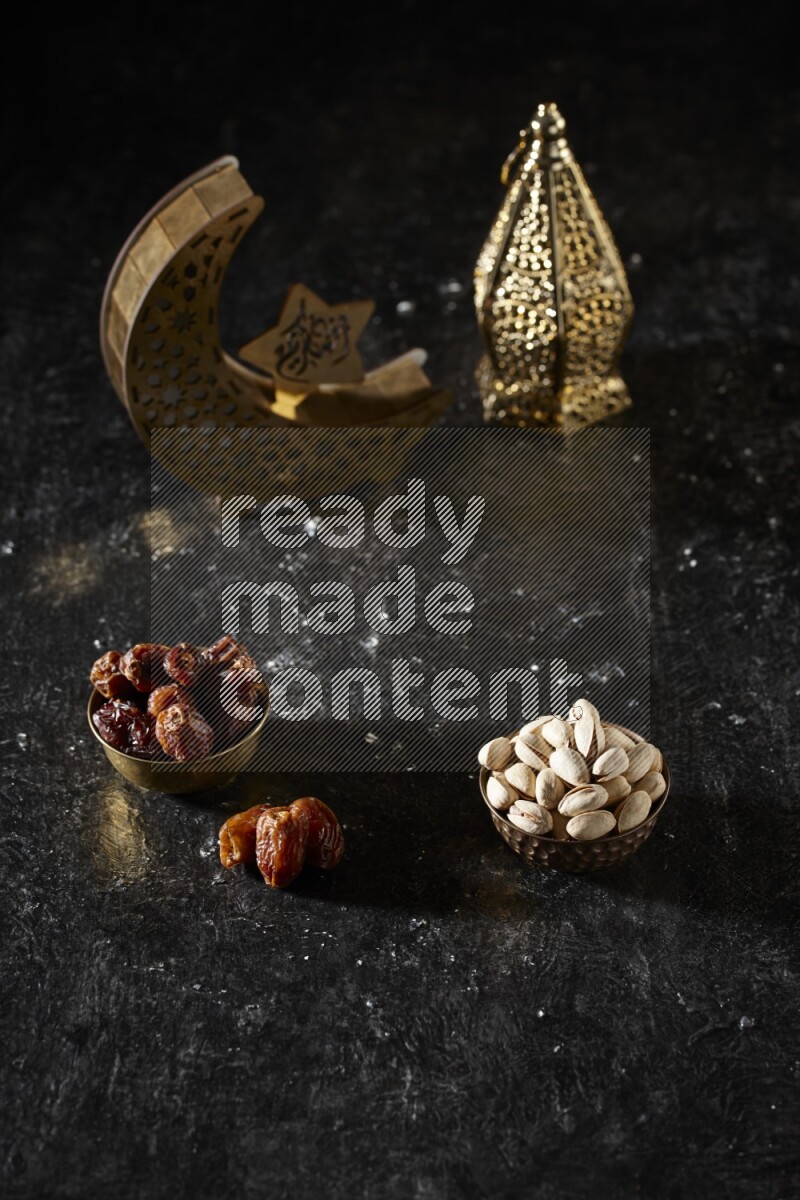 Dates in a metal bowl with pistachios beside golden lanterns in a dark setup
