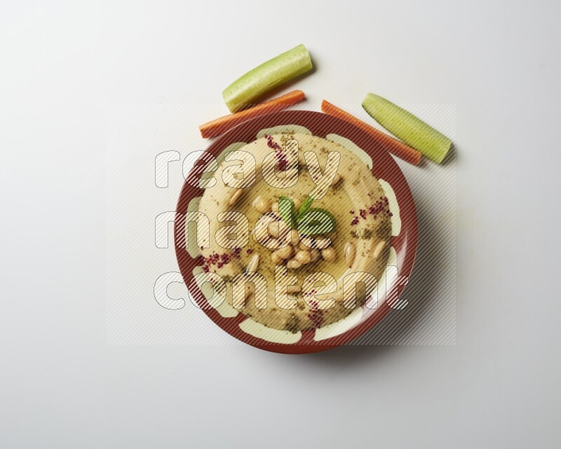 Hummus in a traditional plate garnished with zaatar & sumak on a white background