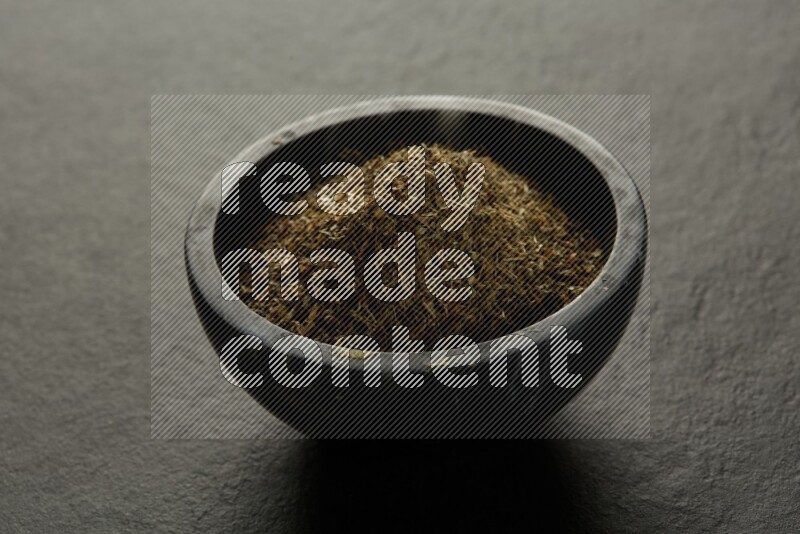 black pottery round sauce bowl filled with herbs on grey textured countertop