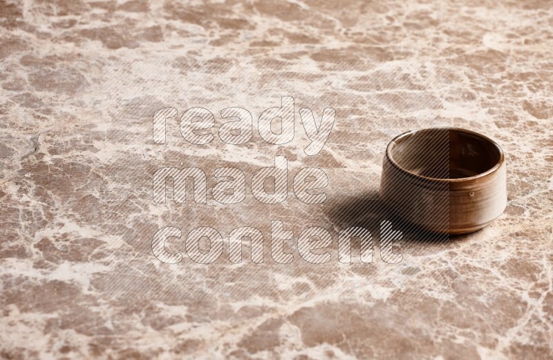 A brown pottery bowl on beige marble background