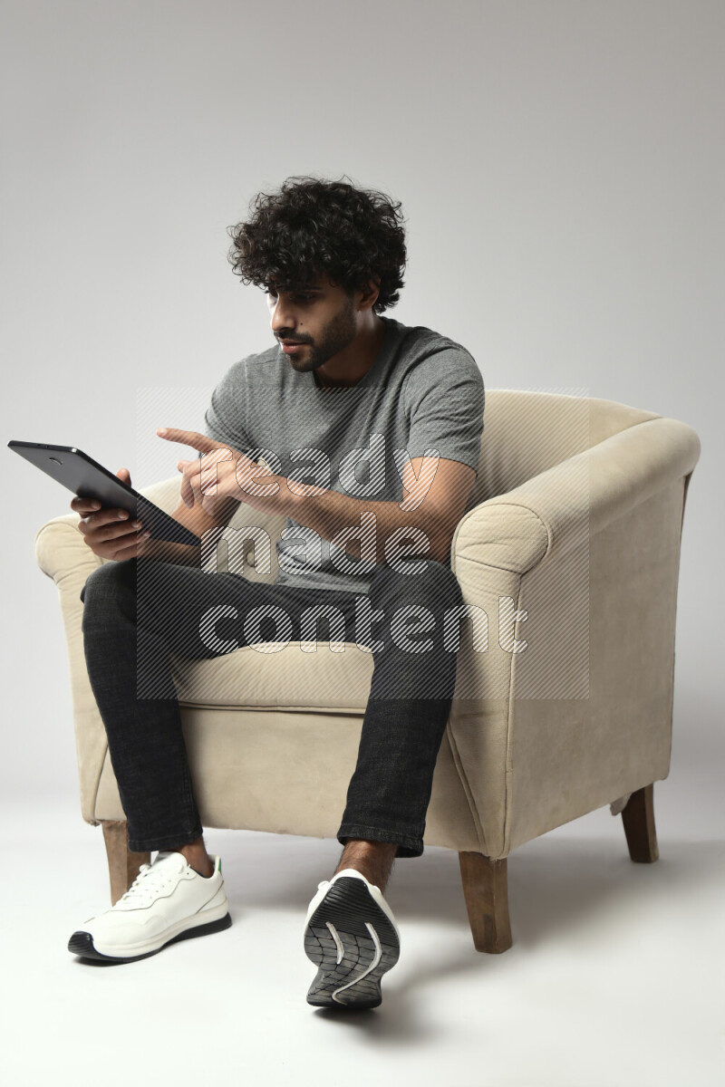 A man wearing casual sitting on a chair browsing on a tablet on white background