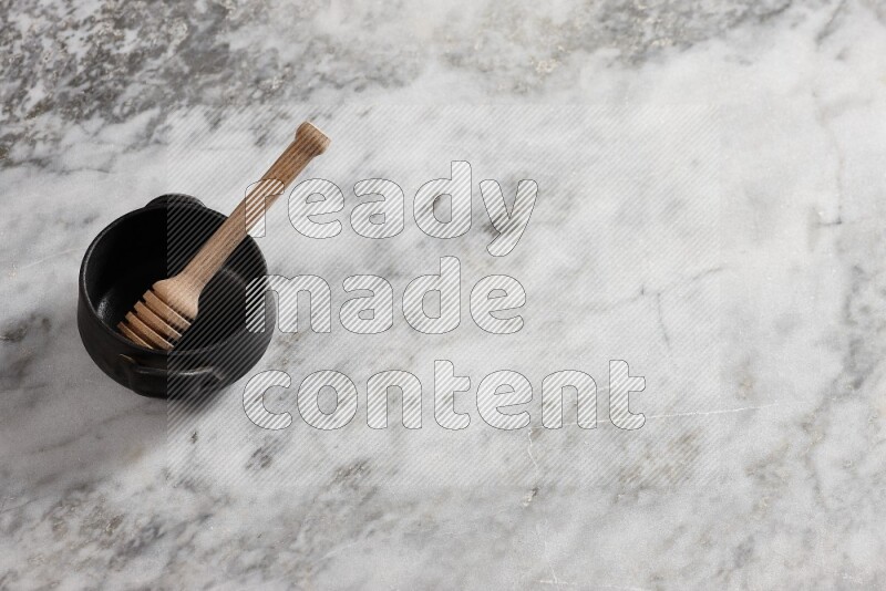 Black pottery bowl with wooden honey dipper in it on grey marble background