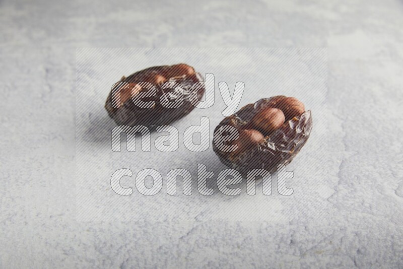 two hazelnuts stuffed madjoul dates on a light grey background