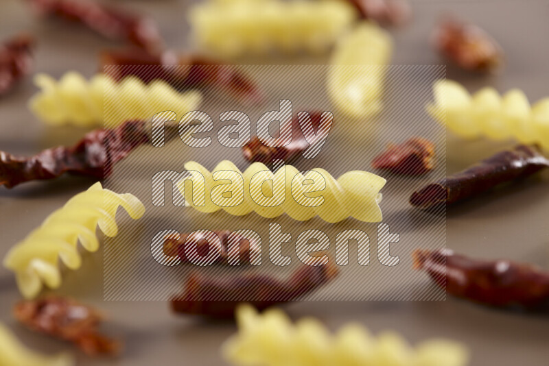 Raw pasta with different ingredients such as cherry tomatoes, garlic, onions, red chilis, black pepper, white pepper, bay laurel leaves, rosemary and cardamom on beige background