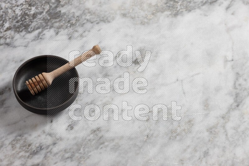 Black pottery bowl with wooden honey dipper in it on grey marble background
