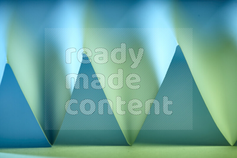 A close-up abstract image showing sharp geometric paper folds in green and blue gradients