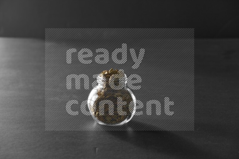 A glass spice jar full of cardamom on black flooring