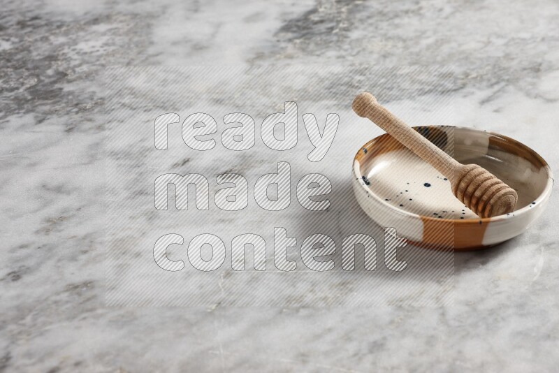 Multicolored pottery bowl with wooden honey dipper in it on grey marble background