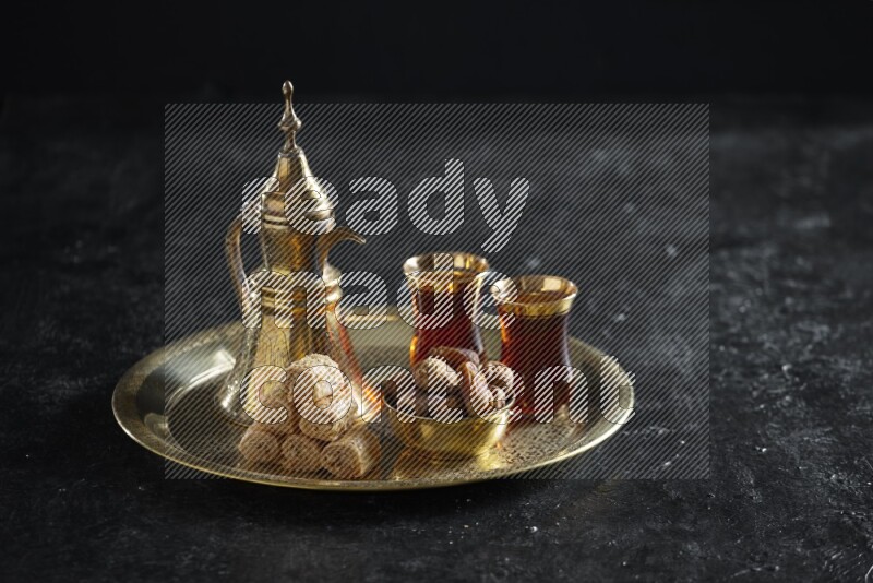 Oriental sweets with dates and a drink on a metal tray in a dark setup