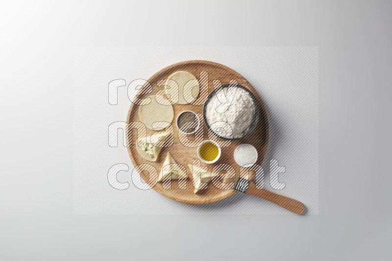two closed sambosas and one open sambosa filled with cheese while flour, salt, black pepper and oil with oil brush aside in a wooden dish on a white background