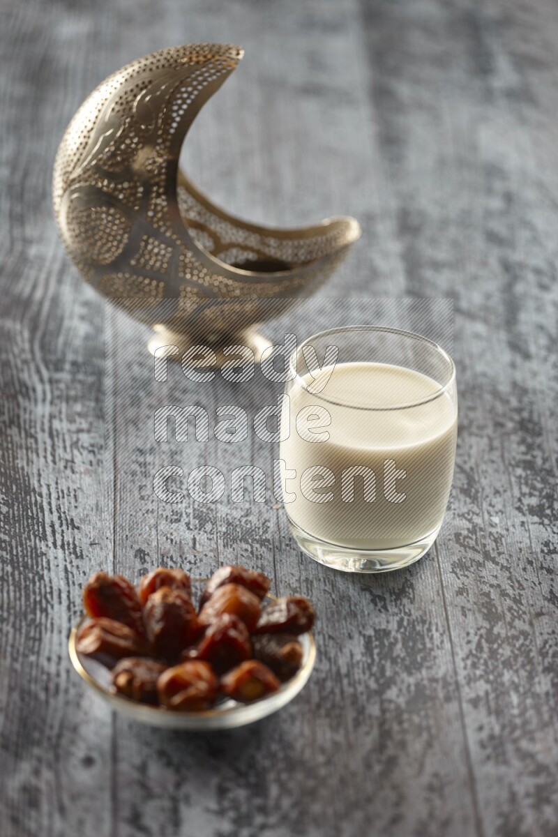 A silver lantern with different drinks, dates, nuts, prayer beads and quran on grey wooden background