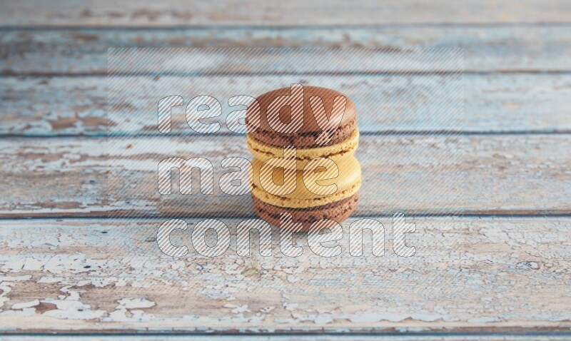 45º Shot of two Yellow and Brown Chai Latte macarons on light blue wooden background