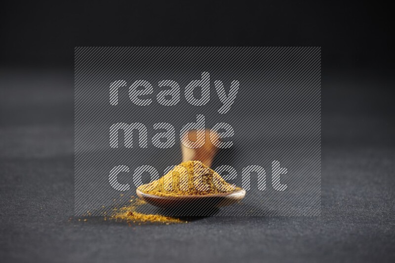 A wooden ladle full of turmeric powder on black flooring