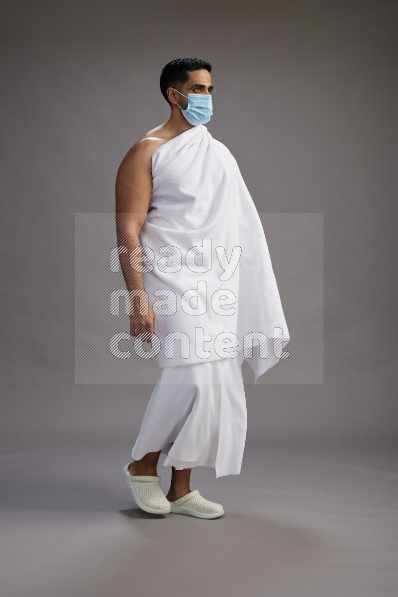 A man wearing Ehram with face mask Standing Interacting with the camera on gray background