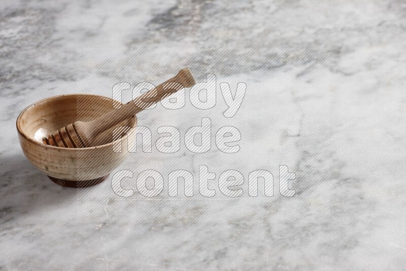 Beige pottery bowl with wooden honey dipper in it on grey marble background
