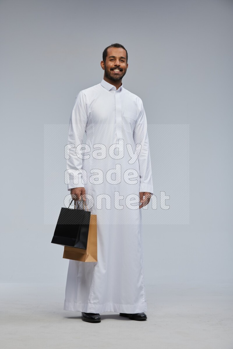 Saudi man Wearing thob standing holding shopping bag on Gray background