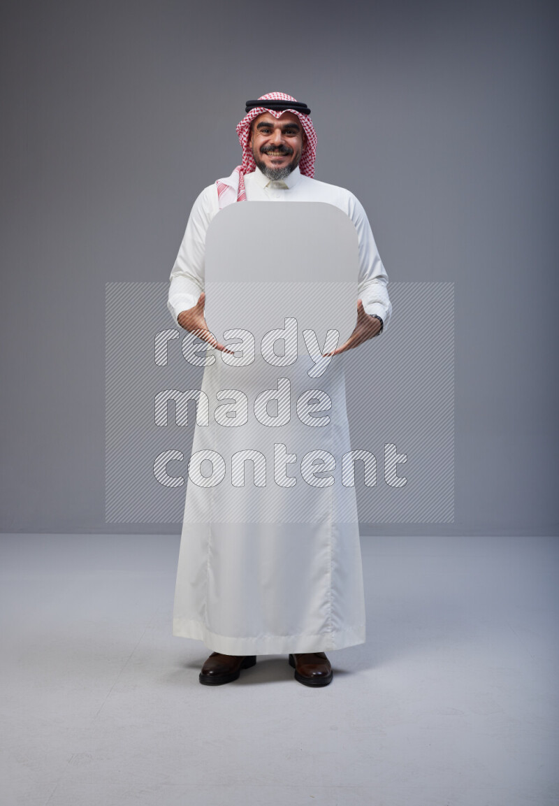 Saudi man Wearing Thob and red Shomag standing holding social media sign on Gray background