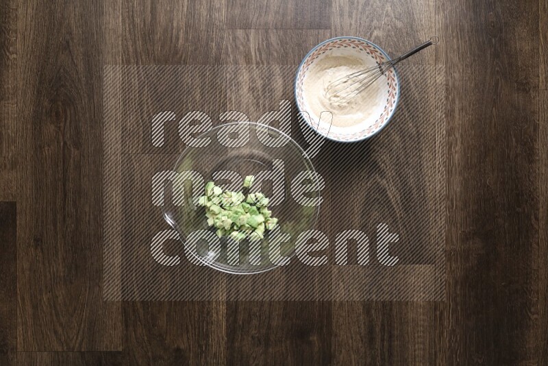 A bowl full of salad (avocado, tomatoes, red beans, olives, bell pepper, corn, lettuce) and bowl of salad dressing on wooden background