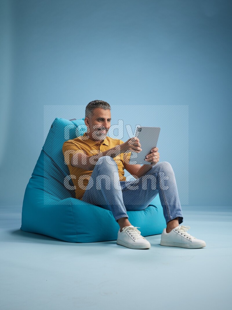 A man sitting on a blue beanbag and working on tablet