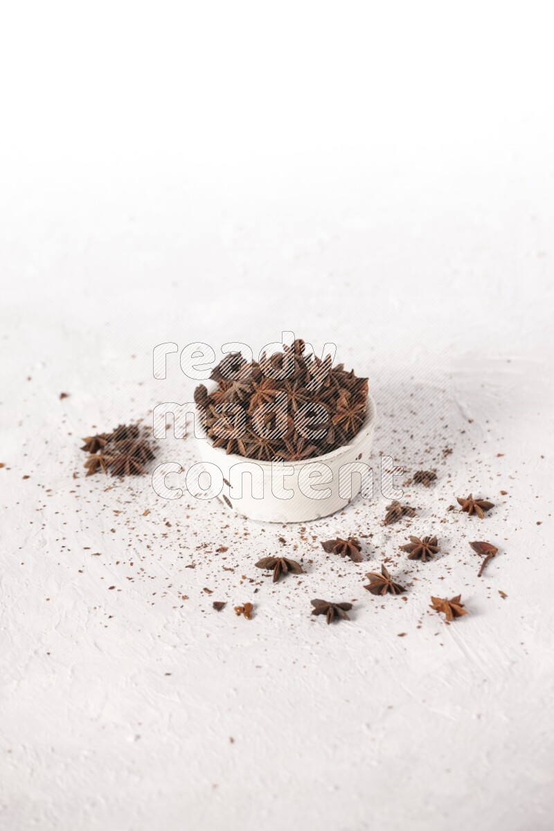 Star Anise in a white bowl and more of it sprinkled on white background