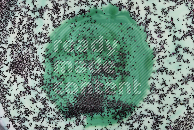 A close-up of sparkling purple glitter scattered on swirling green and white background