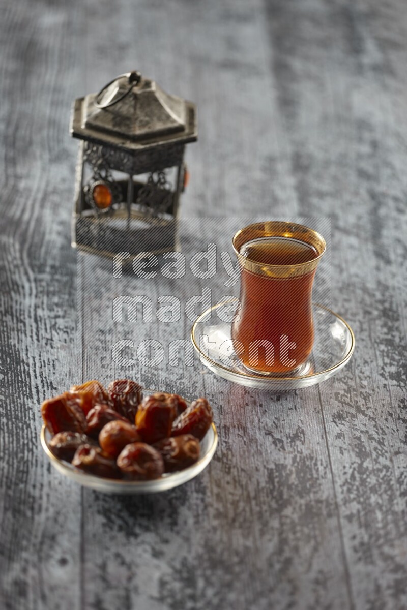 A silver lantern with different drinks, dates, nuts, prayer beads and quran on grey wooden background