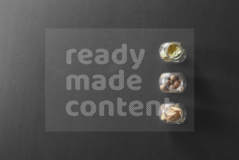 3 glass spice jars full of laurel bay leaves, ginger and nutmeg on black flooring