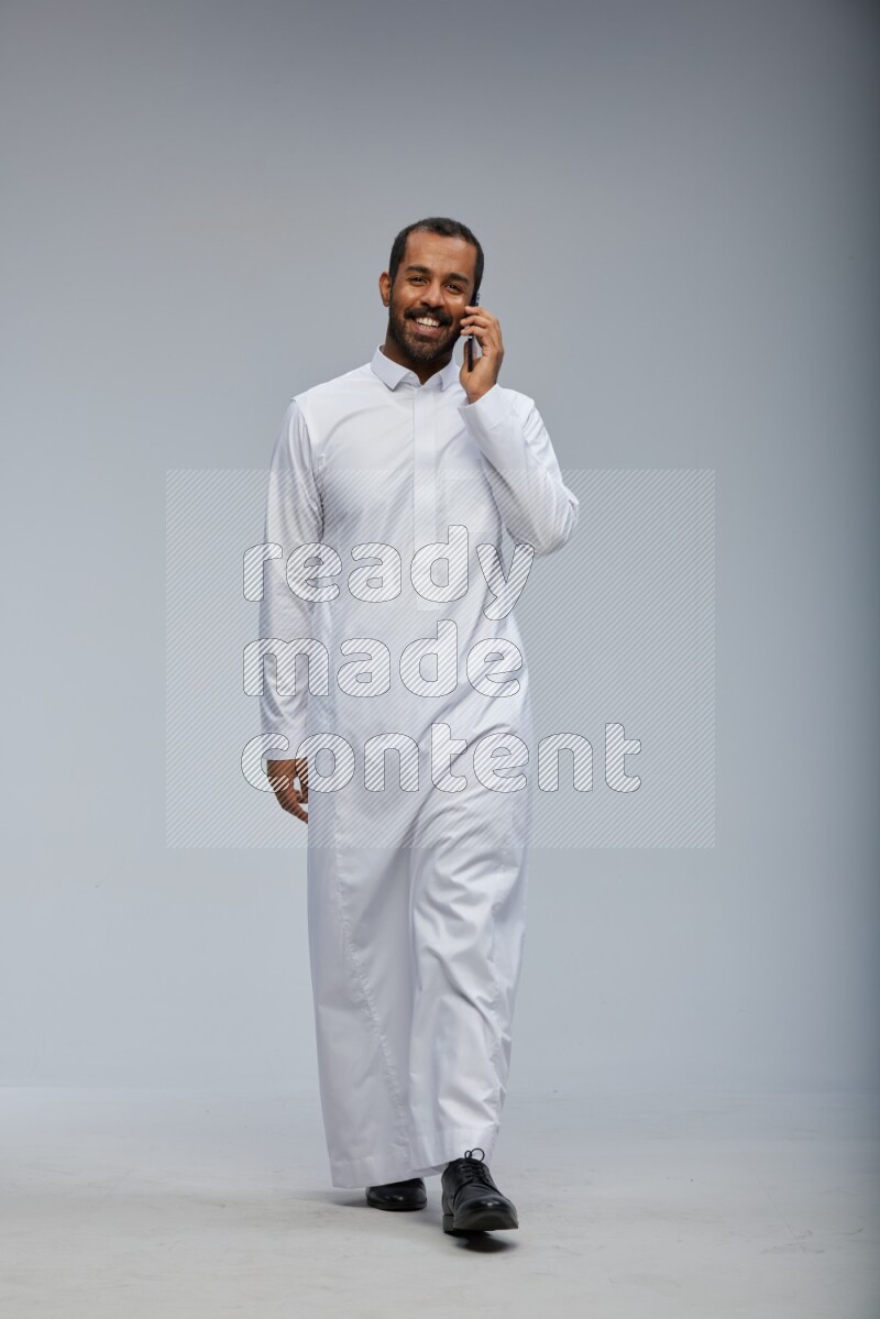 Saudi man wearing Thob standing talking on phone on Gray background