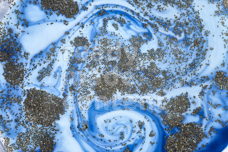 A close-up of sparkling gold glitter scattered on swirling blue background