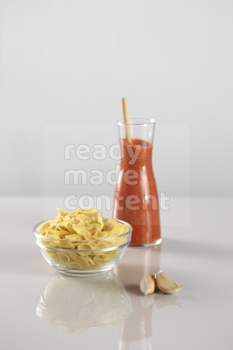 Raw pasta with tomatoe pasta with different ingredients such as cherry tomatoes, basil, garlic, bay laurel, cardamom, white pepper, black pepper, red chilis and wheat stalks on light grey background