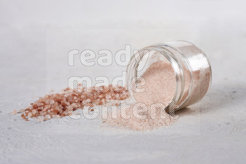 A glass jar full of fine himalayan salt with some himalayan crystals beside it on a white background