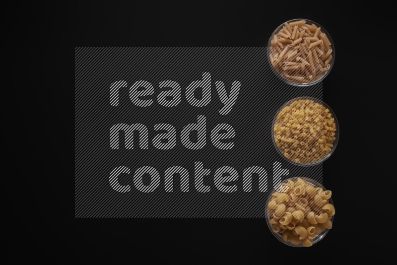 Different pasta types in 3 glass bowls on black background