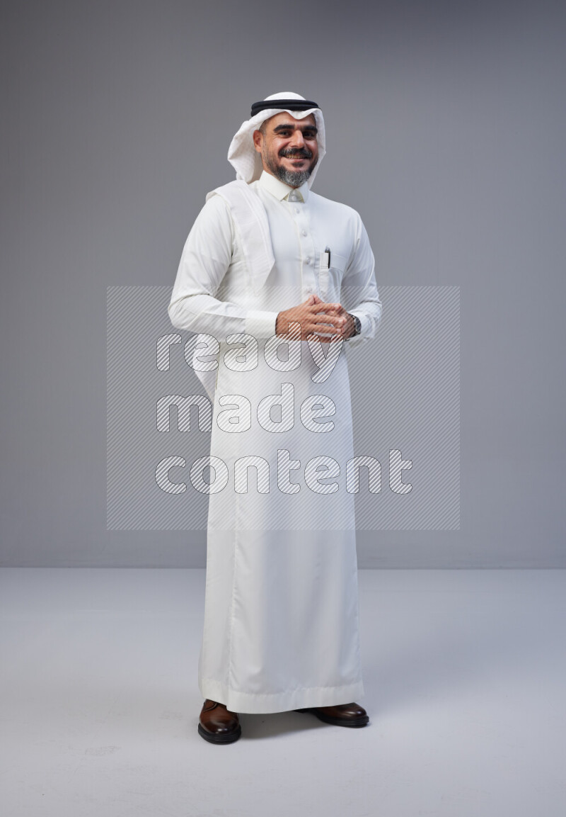 Saudi man Wearing Thob and white Shomag standing interacting with the camera on Gray background
