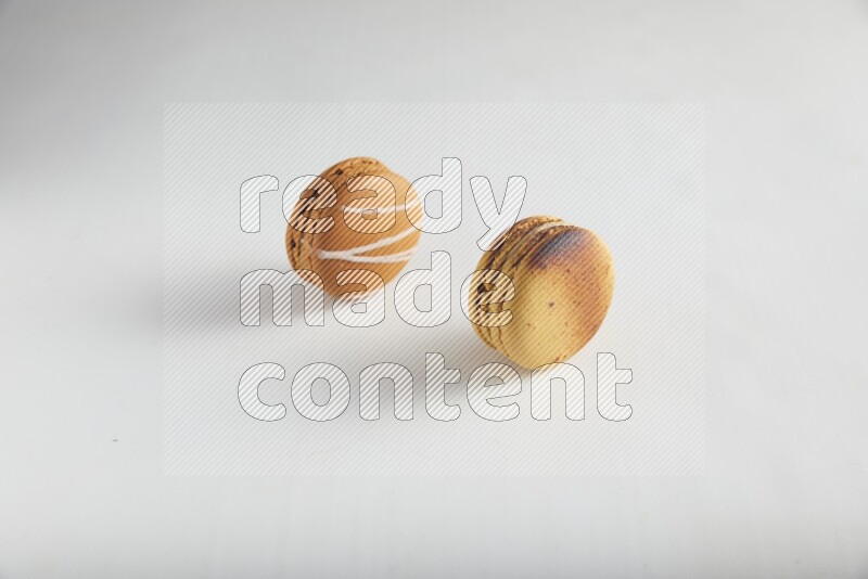 45º Shot of of two assorted Brown Irish Cream, and Yellow Crème Brulée macarons on white background