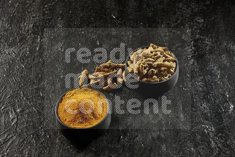 وعاءان من الفخار باللون الأسود، أحدهما ممتلئ ببودرة الكركم والآخر ممتلئ بأصابع كاملة من الكركم المجفف على خلفية سوداء