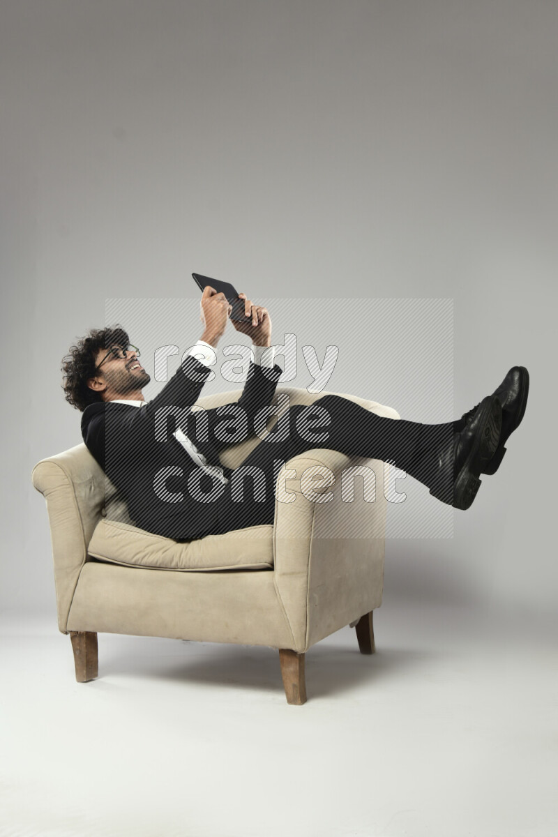 A man wearing formal sitting on a chair gaming on a tablet on white background