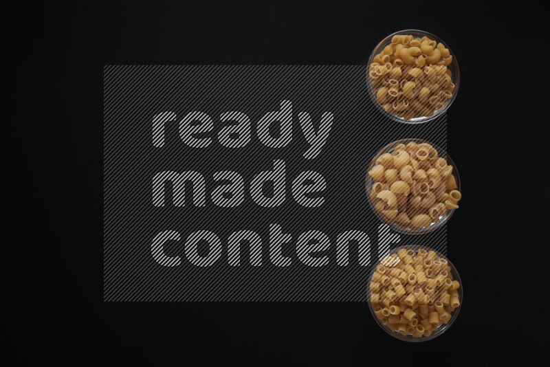 Different pasta types in 3 glass bowls on black background