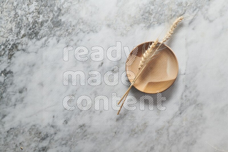 Wheat stalks on multicolored pottery plate on grey marble background