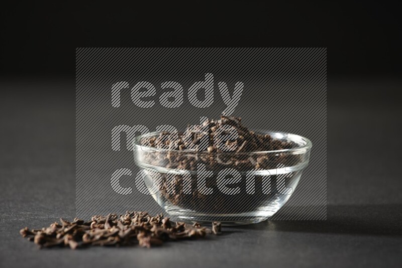 A glass bowl full of cloves on a black flooring