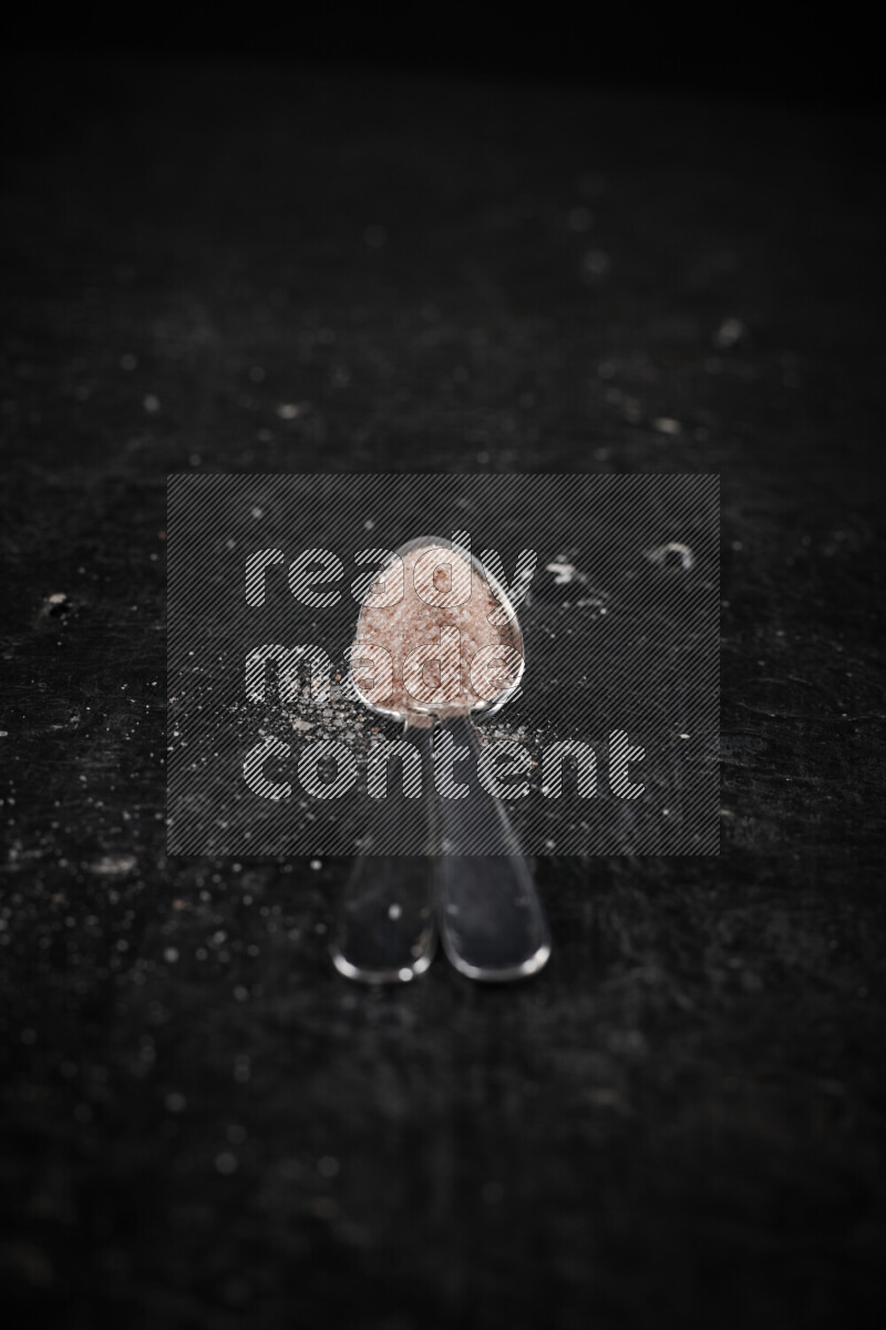 2 metal spoons filled with pink himalayan salt on black background