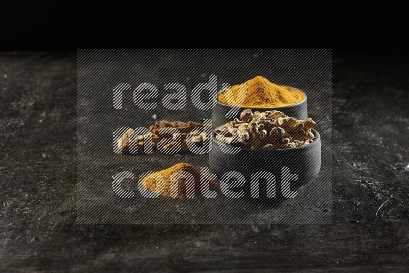 وعاءان من الفخار باللون الأسود، أحدهما ممتلئ ببودرة الكركم والآخر ممتلئ بأصابع كاملة من الكركم المجفف على خلفية سوداء