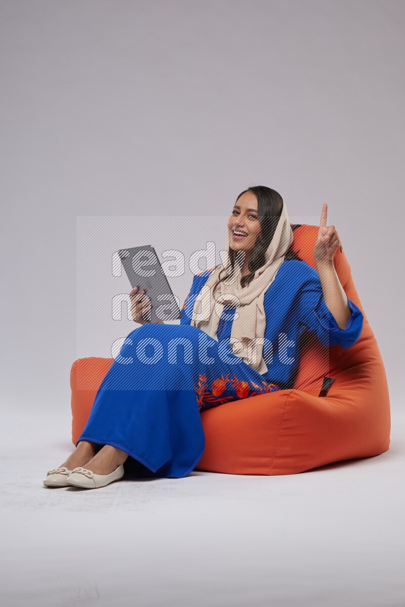A Saudi woman sitting on an orange beanbag and working on tablet